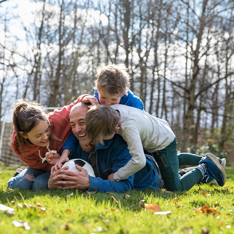 3 kids tackling their dad on a soccer field_480x480