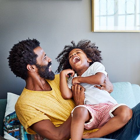 Father laying on bed tickling his young daughter who is laughing