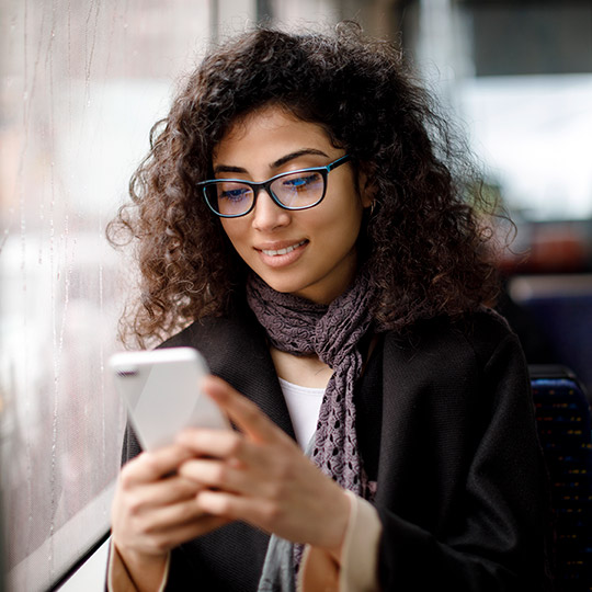 Woman in jacket and scarf looking down at the cell phone in her hands