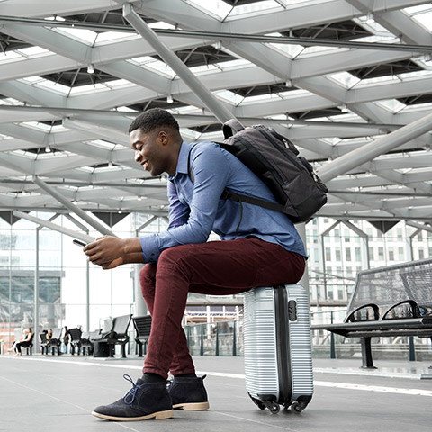Young man sitting on luggage at an airport_hero